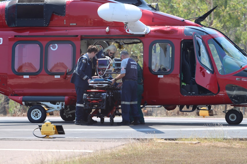A small group of medical staff loaded a person on a stretcher onto a red helicopter parked on a runway.