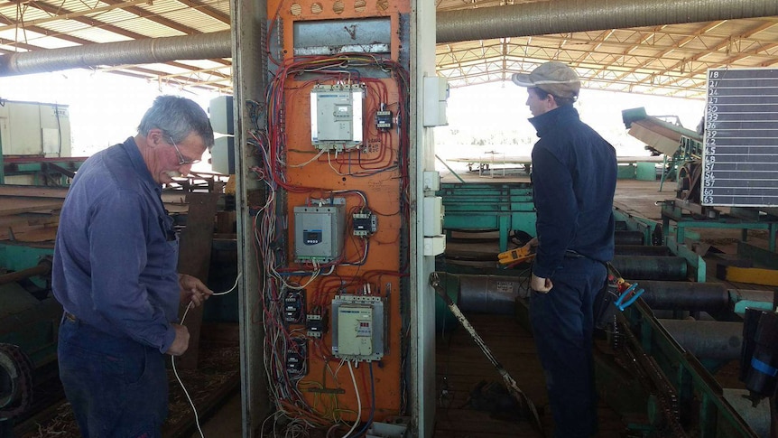 Two electrical tradesmen are working on wires connected to the sawmills operating system.