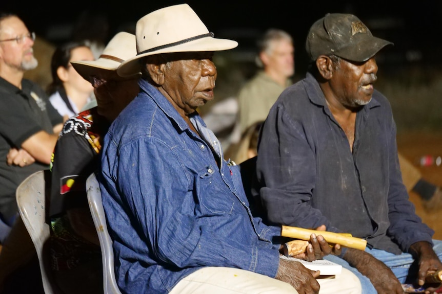 An older Indigenous man sits with clapping sticks