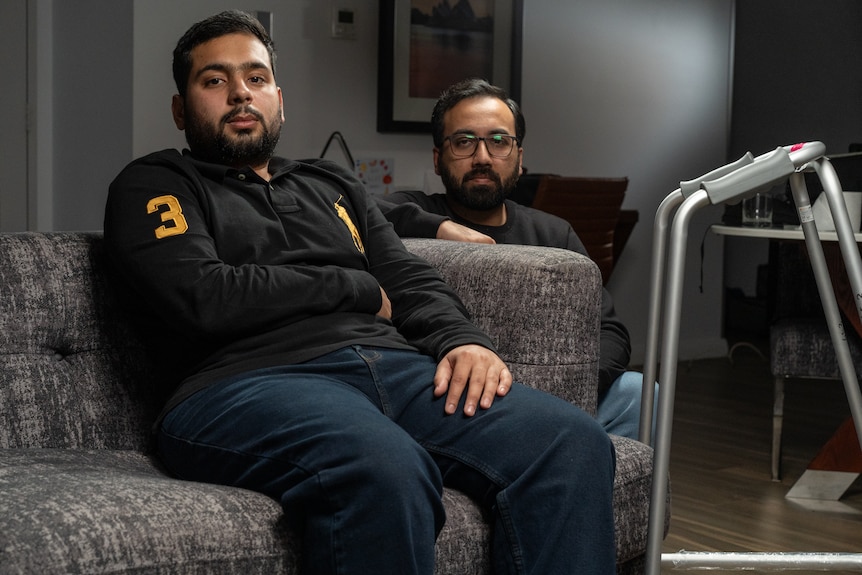 Muhammad Taha sitting on a grey couch while his friend Muhammad Fahad kneels beside him.