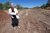 A woman stands in an area of cleared bushland.