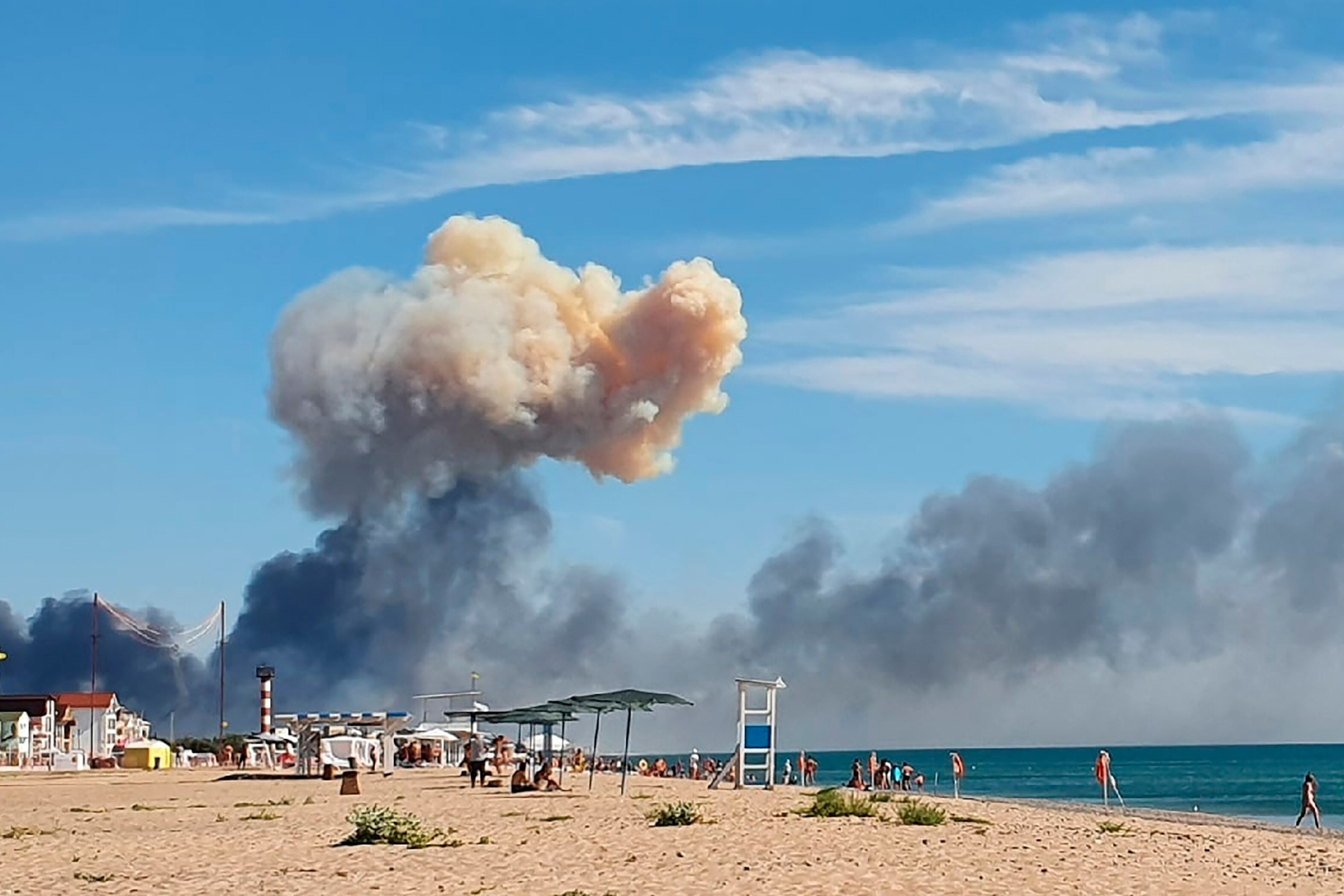 People walk along the beach with a giant cloud of smoke behind them