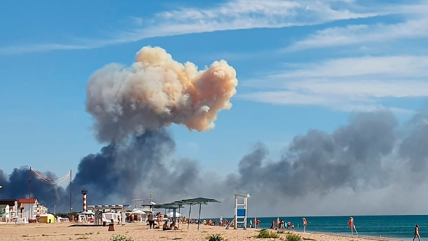 People walk along the beach with a giant cloud of smoke behind them
