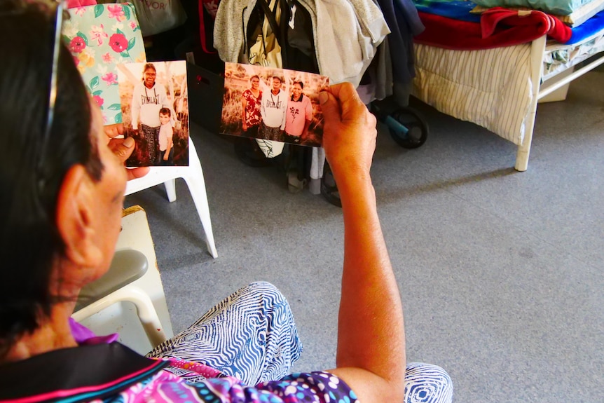 Aboriginal woman holds up pictures of her family. 