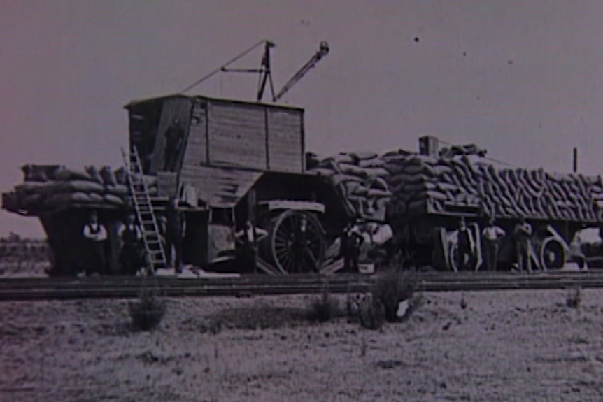 Black and white photo of giant tractor loaded with bags of wheat