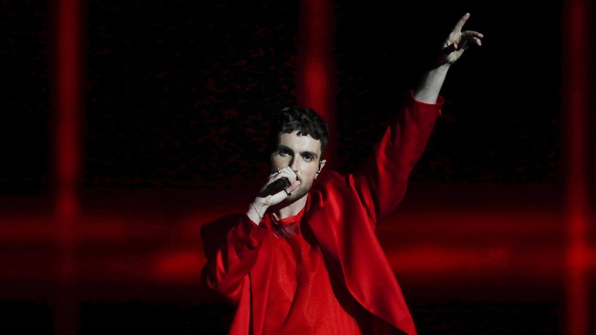 A performer in a red outfit gestures while singing at a Eurovision Song Contest semi-final. 