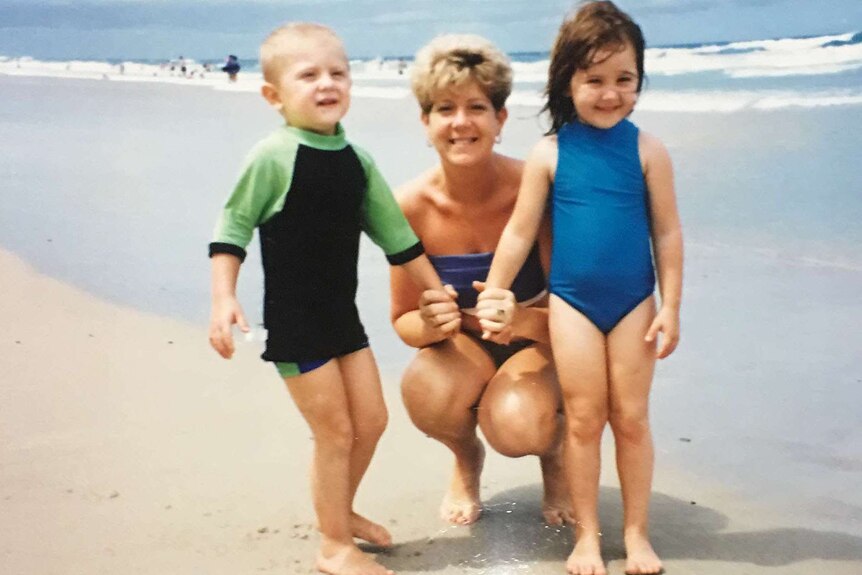 Tanya Battel crouches on a beach with her two children.