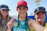 An Australian female athlete holds a World Triathlon Para Championships gold medal while next to two supporters.