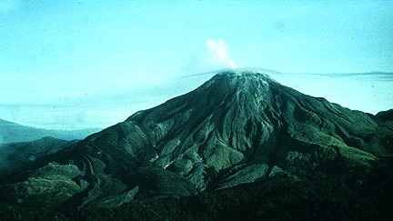 Wide shot of a conical volcano with smoke coming out of it.