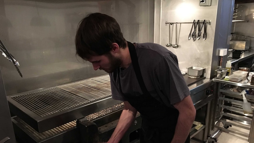 A chef leans over a grill in a restaurant