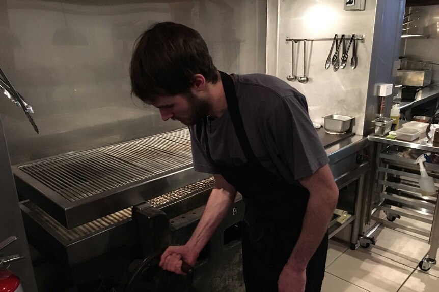 A chef leans over a grill in a restaurant