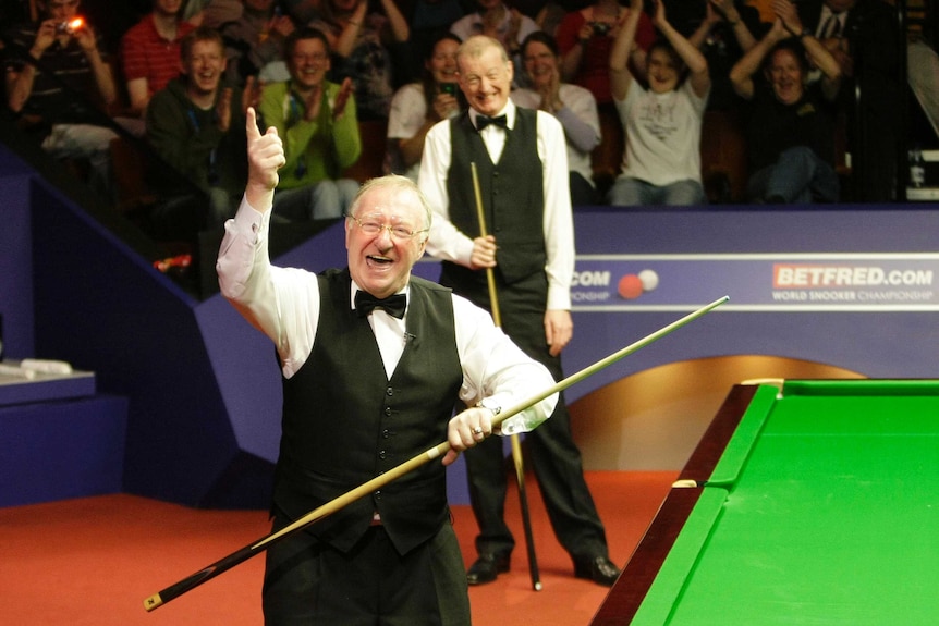 Dennis Taylor smiles and waves his right hand above his head as Steve Davis stands in the background