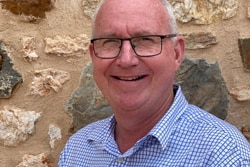 Chris Heinjus standing in front of brick wall smiling.