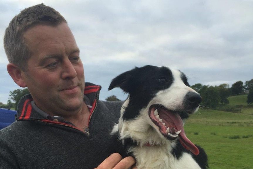 James Rebanks stands holding his pet dog which has its tongue out