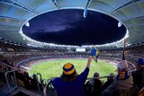 A fisheye shot of a full Perth Stadium at night, with a fan waving an Eagles flag in the foreground