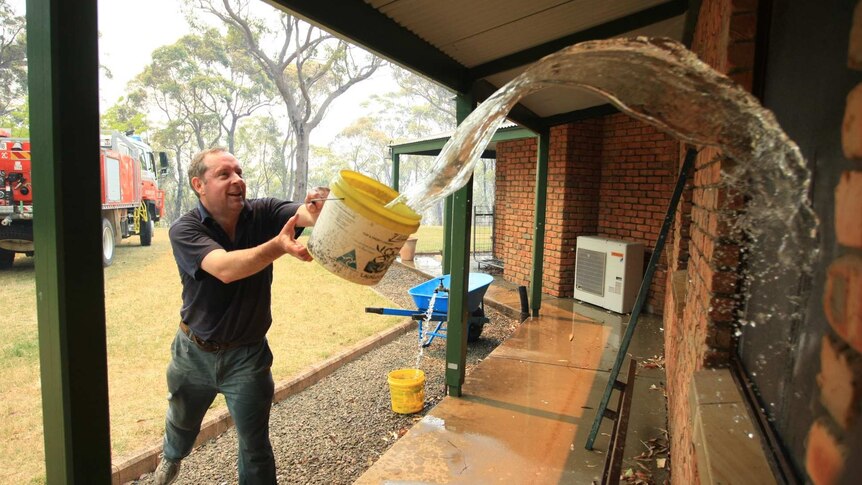 Mark Wilson throws water over his house in Faulconbridge in the Blue Mountains.