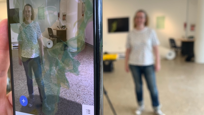 A phone screen captures artist Nat Ord with some augmented reality around her.