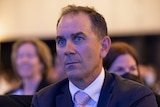 Justin Langer sits in a suit listening at the Leadership Matters breakfast with former PM John Howard