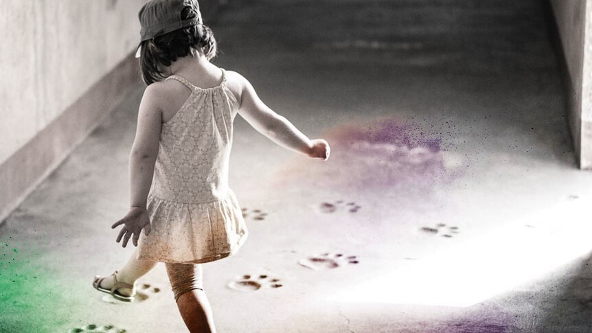 A photograph of a young child in a white dress and grey cap, dancing between paw prints on the ground.