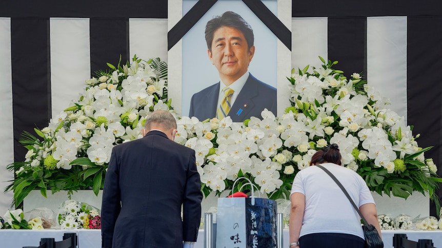 People leave flowers and bow towards a large photograph of assasinated Japanese leader Shinzo Abe.