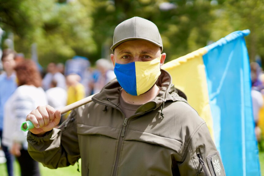 A man wears a Ukranian face mask and holds a Ukranian flag at a rally 
