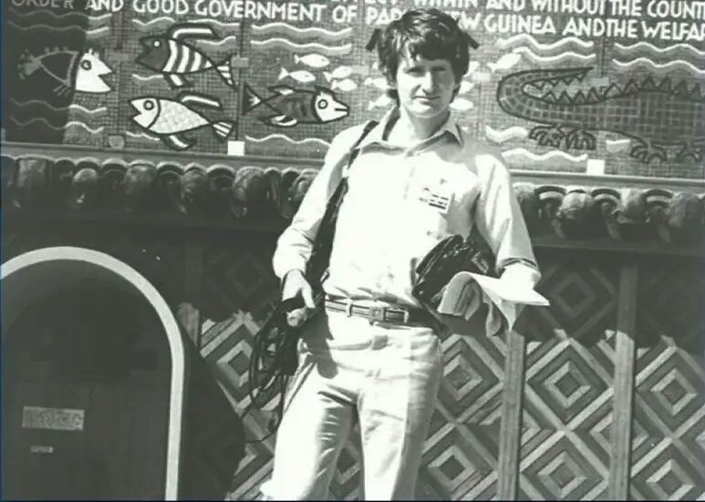 Black and white photo of young Dorney with tape recorder standing in front of PNG building.
