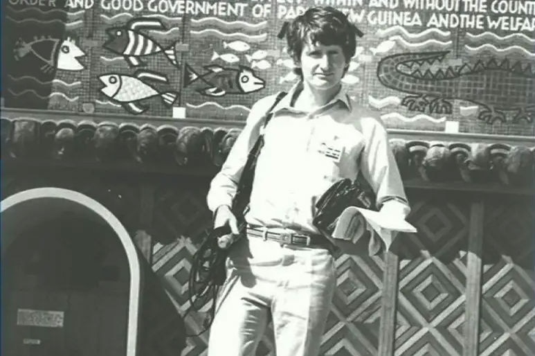 Black and white photo of young Dorney with tape recorder standing in front of PNG building.