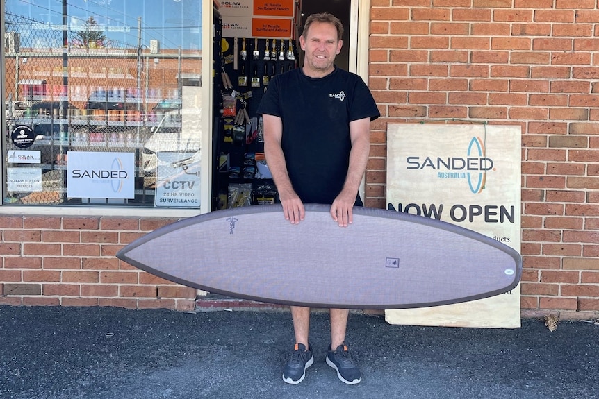 man holding grey brown board in front of a brick shop front