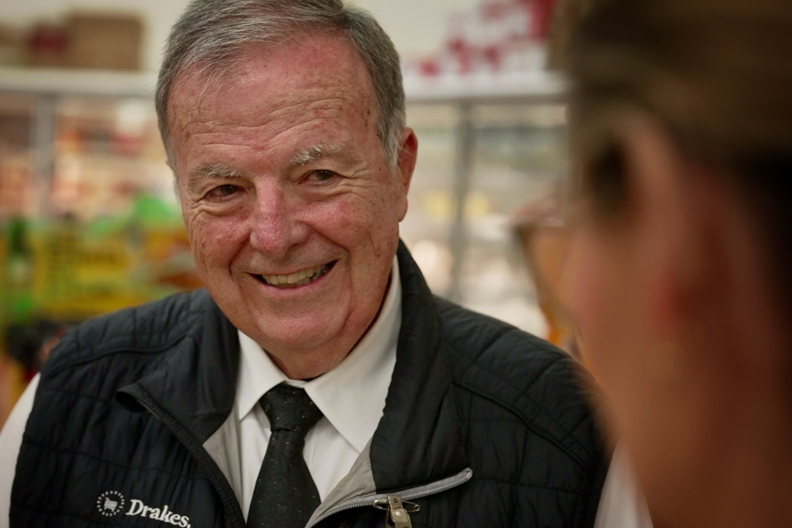 an older supermarket worker smiles at a colleague