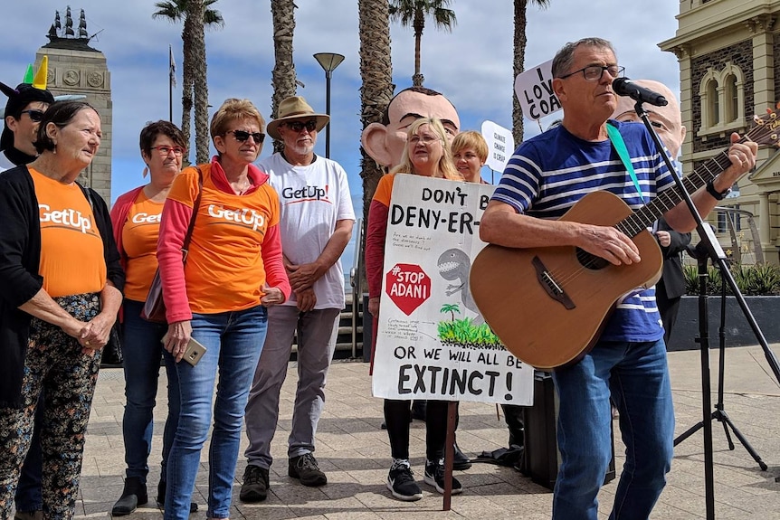 A man playing a guitar sings with protesters behind