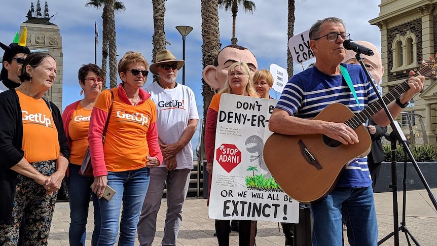 A man playing a guitar sings with protesters behind