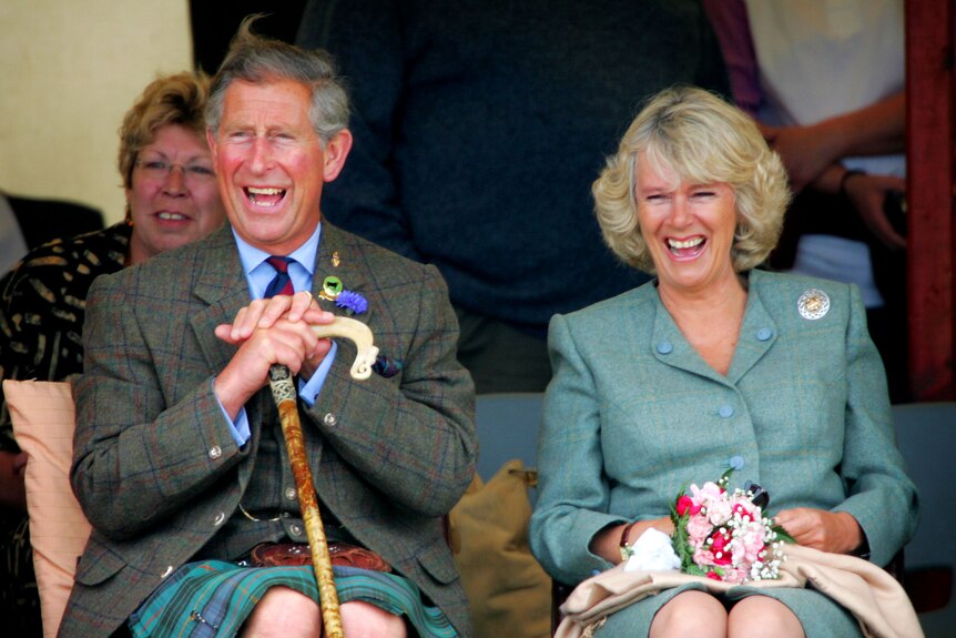 Charles in a kilt sits next to Camilla, both are laughing 