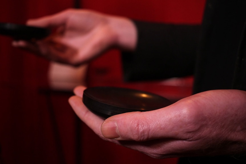 A person holds two small, round black objects.