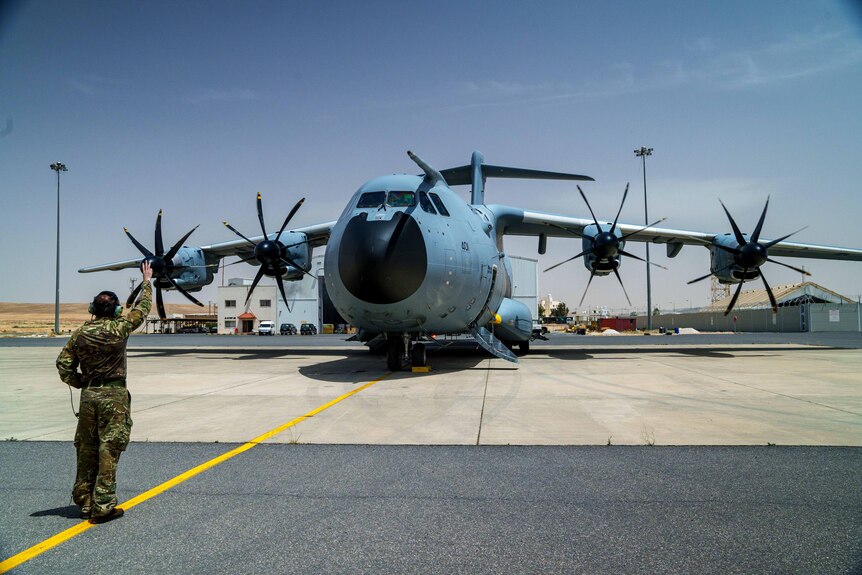 Two men walk towards an A400 military plane parked in a desert