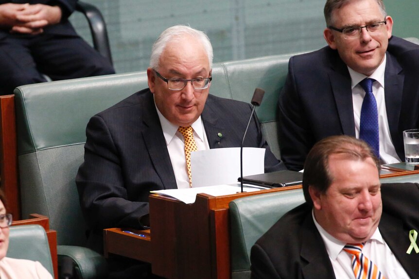 Danby is wearing a yellow tie, holding a piece of paper, looking towards the government benches.