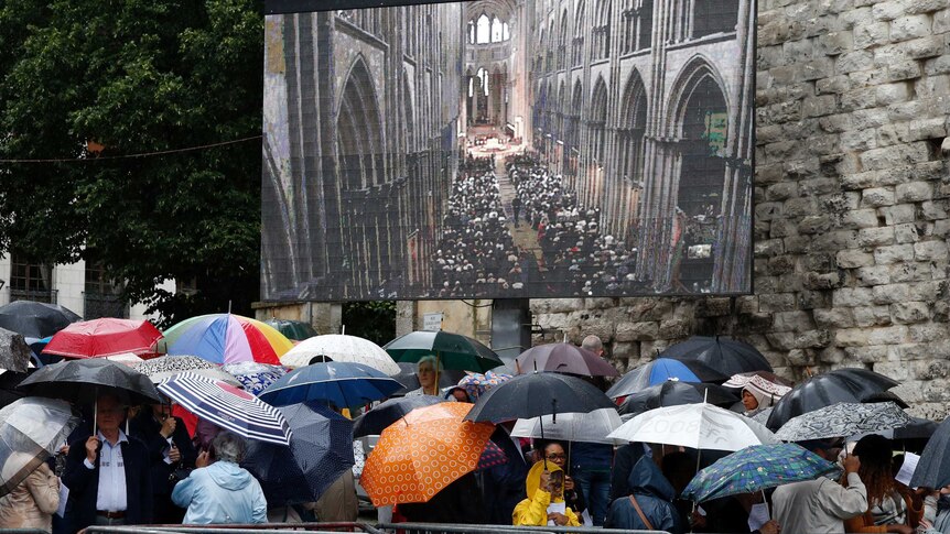 Mourners gather in the rain near a giant screen outside the Cathedral in Rouen