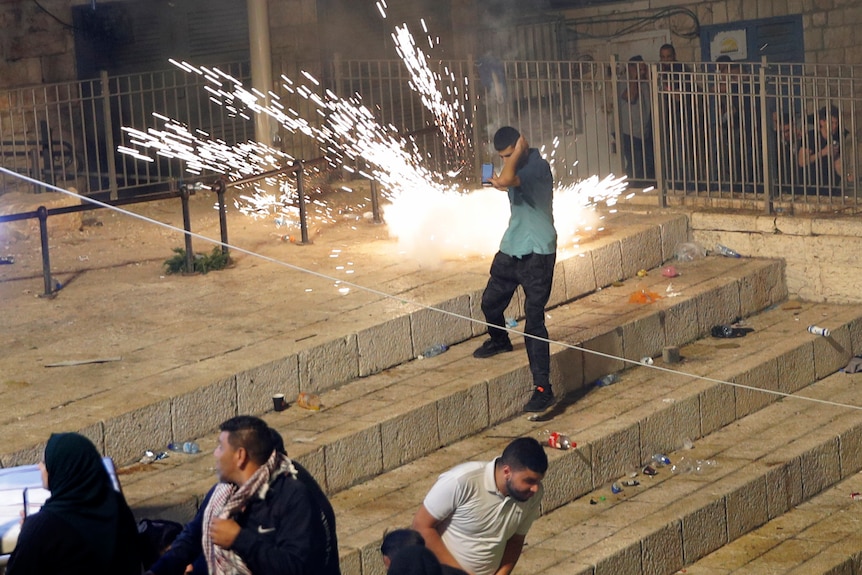 A man holds his head as an explosion goes off