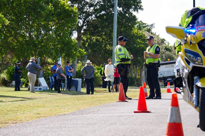 Police talk in the foreground, with plastic chairs for the funeral in the background.