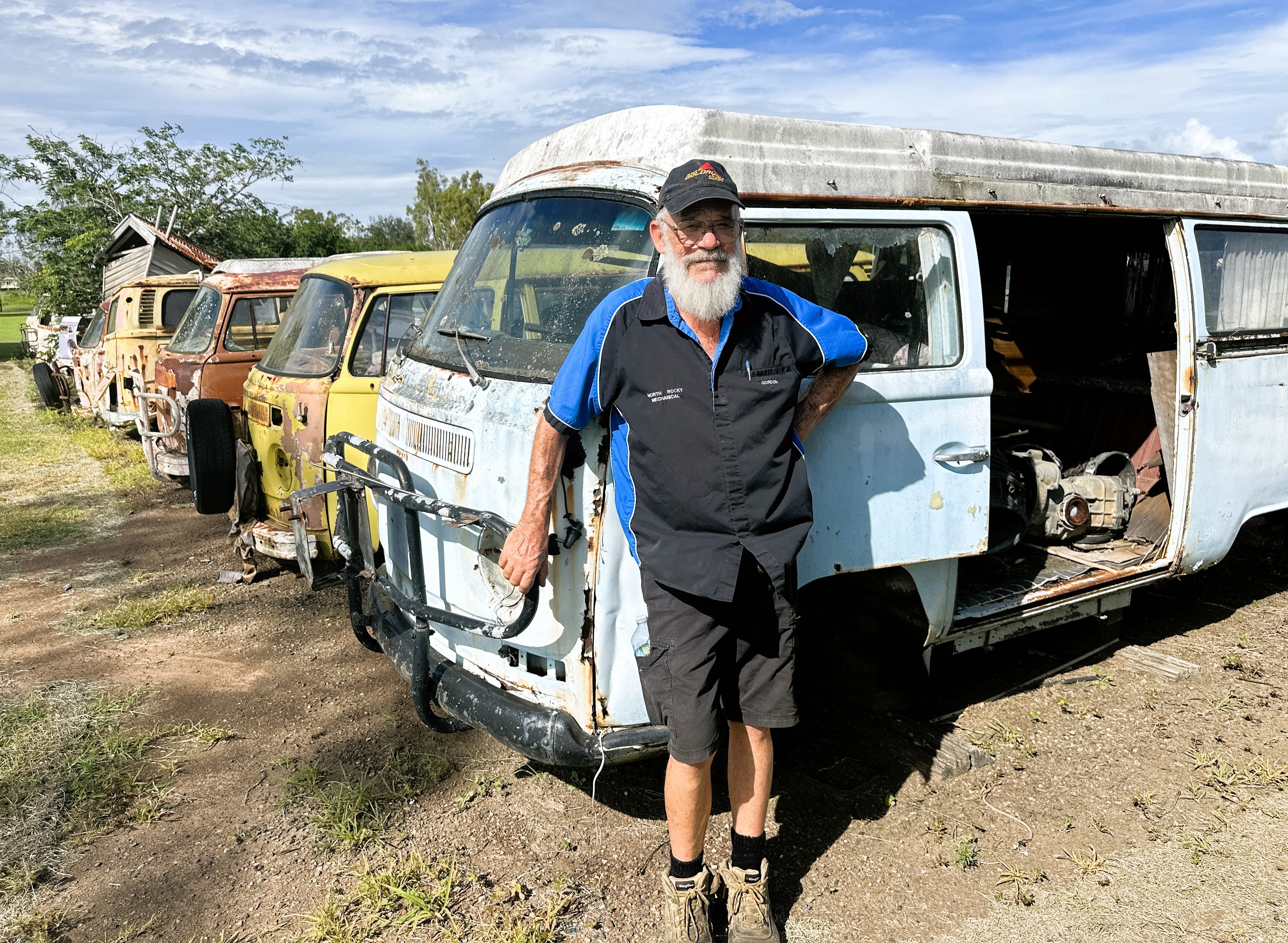 A man in his backyard garage full of old Volkswagen vehicles.