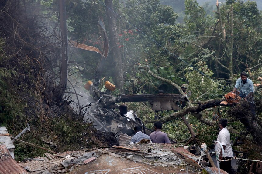 People stand near the debris of a helicopter that crashed in a forested area