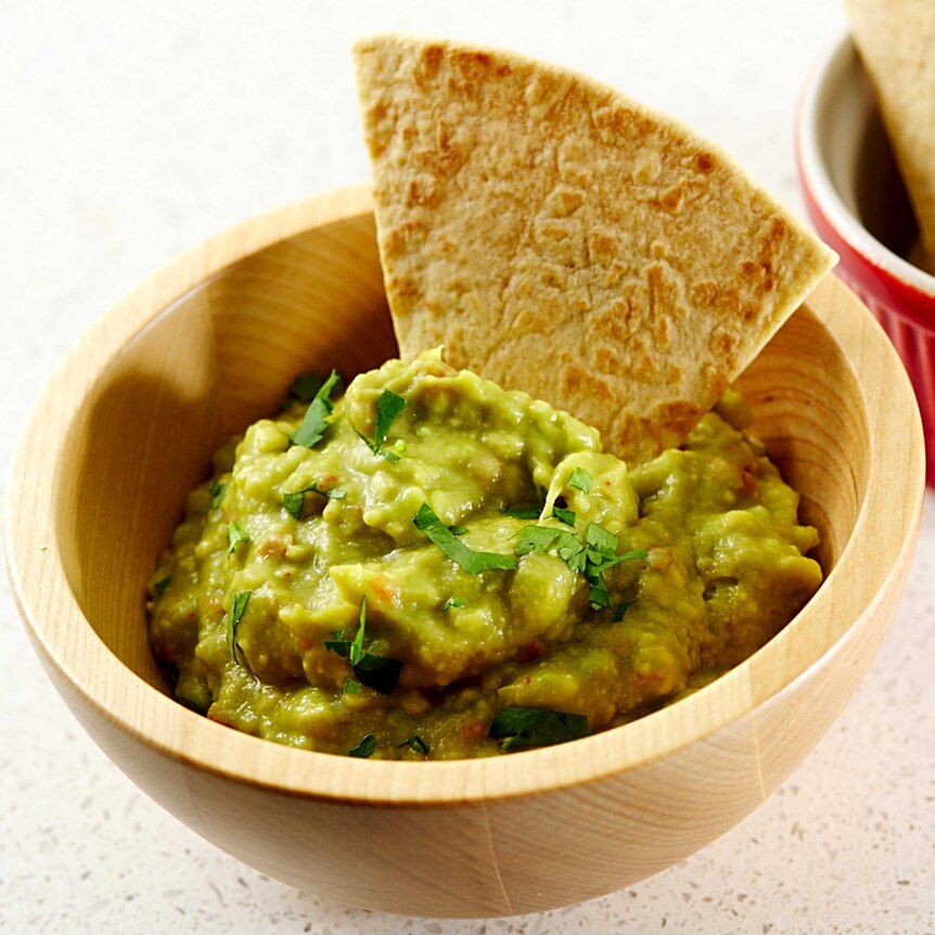 A bowl of guacamole with corn chips on the side.