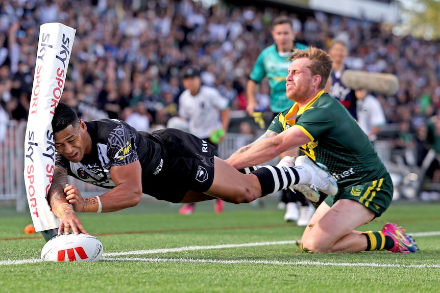 A Kiwis player scores a try in the corner as a Kangaroos opponent attempts a tackle.