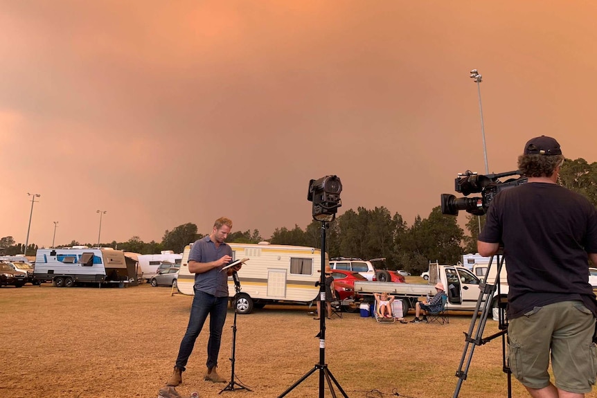 Macdonald standing in front of camera with caravans in background under red smoky sky.