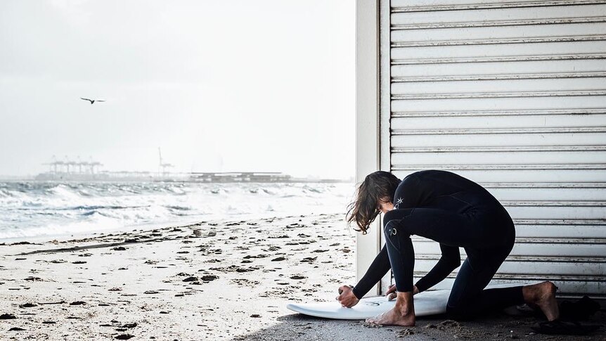 A person prepares their surfboard on a beach.