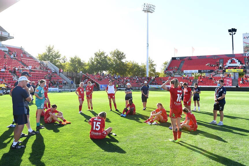 Soccer players wearing red gather in a circle, some sitting down and some standing up