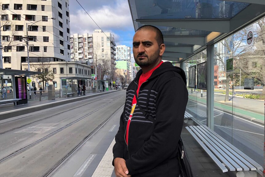 A man stands at a tram stop in Melbourne.