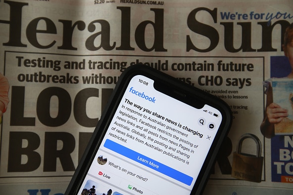 An iPhone is placed on a copy of the Herald Sun with Facebook open.