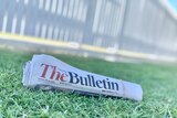 A rolled up copy of the Morning Bulletin newspaper sits on a green grass lawn.