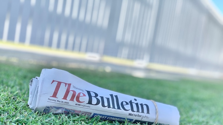 A rolled up copy of the Morning Bulletin newspaper sits on a green grass lawn.