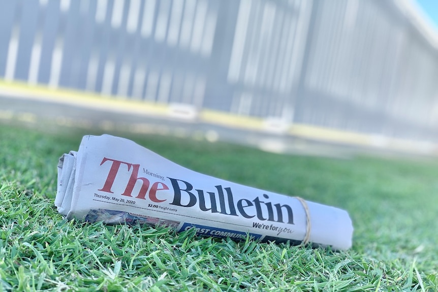A rolled up copy of the Morning Bulletin newspaper sits on a green grass lawn.